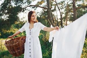 jeune femme au foyer avec panier dans les mains raccroche un chiffon blanc propre et lavé pour sécher photo