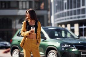 avec boisson dans les mains. jeune femme à la mode en manteau de couleur bordeaux pendant la journée avec sa voiture photo