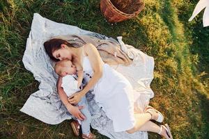 couché sur le drap blanc. jeune mère avec son petit fils est à l'extérieur dans la forêt. beau soleil photo