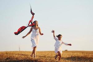 mère heureuse avec sa petite fille s'amuser en jouant avec le cerf-volant à l'extérieur sur le terrain photo