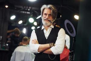 en salon de coiffure. homme âgé moderne et élégant aux cheveux gris et à la barbe est à l'intérieur photo