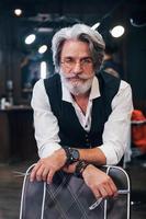 dans des vêtements rétro dans un salon de coiffure. homme âgé moderne et élégant aux cheveux gris et à la barbe est à l'intérieur photo