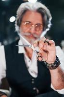 est assis sur la chaise du salon de coiffure. homme âgé moderne et élégant aux cheveux gris et à la barbe est à l'intérieur photo