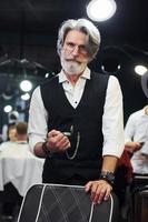 dans des vêtements rétro dans un salon de coiffure. homme âgé moderne et élégant aux cheveux gris et à la barbe est à l'intérieur photo