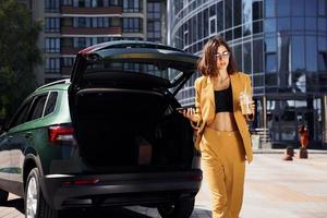 immeuble d'affaires moderne à l'arrière-plan. jeune femme à la mode en manteau de couleur bordeaux pendant la journée avec sa voiture photo