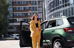 marche en avant de l'automobile. jeune femme à la mode en manteau de couleur bordeaux pendant la journée avec sa voiture photo