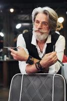 dans des vêtements rétro dans un salon de coiffure. homme âgé moderne et élégant aux cheveux gris et à la barbe est à l'intérieur photo