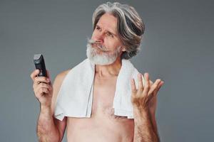 prendre soin de la barbe. homme âgé moderne et élégant aux cheveux gris est à l'intérieur photo