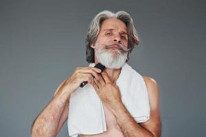 prendre soin de la barbe. homme âgé moderne et élégant aux cheveux gris est à l'intérieur photo