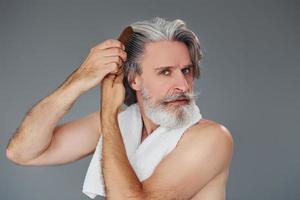 prendre soin de la clarté du visage et de la peau. homme âgé moderne et élégant aux cheveux gris et à la barbe est à l'intérieur photo