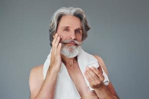 prendre soin de la clarté du visage et de la peau. homme âgé moderne et élégant aux cheveux gris et à la barbe est à l'intérieur photo