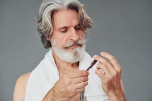 prendre soin de la barbe. homme âgé moderne et élégant aux cheveux gris est à l'intérieur photo