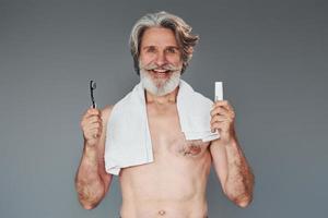 à l'aide de dentifrice. homme âgé moderne et élégant aux cheveux gris et à la barbe est à l'intérieur photo