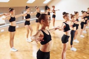 debout dans la rangée. groupe d'enfants féminins pratiquant des exercices athlétiques ensemble à l'intérieur photo