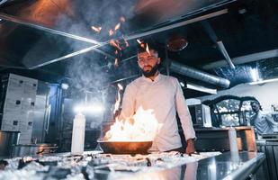 utilise une poêle à frire. chef en uniforme blanc cuisinant des aliments à la cuisine. journée bien remplie au travail photo