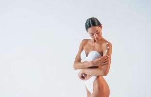 met de la crème sur la peau. belle femme avec un corps mince en sous-vêtements est en studio photo