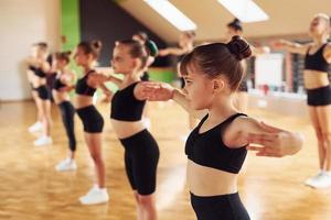 debout dans la rangée. groupe d'enfants féminins pratiquant des exercices athlétiques ensemble à l'intérieur photo