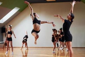 femme enseignant et aidant. groupe d'enfants féminins pratiquant des exercices athlétiques ensemble à l'intérieur photo