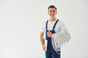 contient des câbles, un bloc-notes et un tournevis. travailleur masculin en uniforme bleu debout à l'intérieur du studio sur fond blanc photo