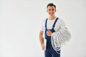 contient des câbles, un bloc-notes et un tournevis. travailleur masculin en uniforme bleu debout à l'intérieur du studio sur fond blanc photo