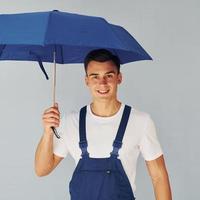 tient le parapluie à la main. travailleur masculin en uniforme bleu debout à l'intérieur du studio sur fond blanc photo