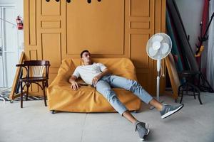 jeune homme avec une coupe de cheveux élégante et dans des vêtements décontractés assis à l'intérieur dans une chambre avec un intérieur de couleur orange photo