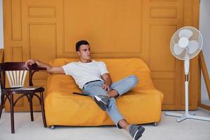 jeune homme avec une coupe de cheveux élégante et dans des vêtements décontractés assis à l'intérieur dans une chambre avec un intérieur de couleur orange photo