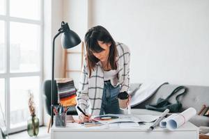 debout près de la table. la jeune travailleuse indépendante est à l'intérieur de la maison pendant la journée photo