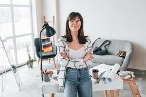 debout près de la table. la jeune travailleuse indépendante est à l'intérieur de la maison pendant la journée photo