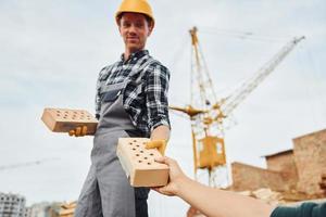 prend la brique d'un autre gars. ouvrier du bâtiment en uniforme et équipement de sécurité a un travail sur le bâtiment photo