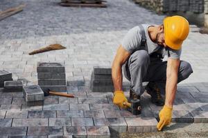 utilise un marteau en caoutchouc. travailleur masculin en uniforme de couleur jaune a un emploi avec la chaussée photo