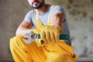 tient la clé à la main. travailleur en uniforme de couleur jaune installant un système de chauffage par le sol photo