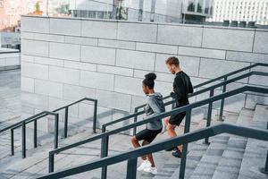 courir sur les gradins. un homme européen et une femme afro-américaine en vêtements sportifs s'entraînent ensemble photo