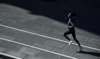 coureur rapide. une jeune femme afro-américaine en vêtements sportifs s'entraîne à l'extérieur pendant la journée photo