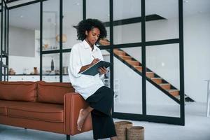 tient le bloc-notes. jeune femme afro-américaine aux cheveux bouclés à l'intérieur à la maison photo