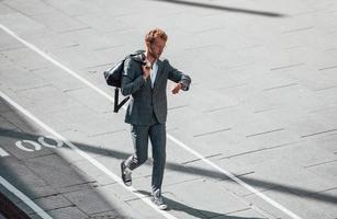 marche sur la route. jeune homme d'affaires en tenue de soirée grise est à l'extérieur de la ville photo