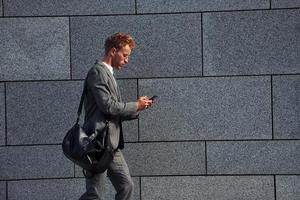 contre le mur gris. jeune homme d'affaires en tenue de soirée grise est à l'extérieur de la ville photo