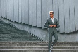 posant pour un appareil photo. jeune homme d'affaires en tenue de soirée grise est à l'extérieur de la ville photo