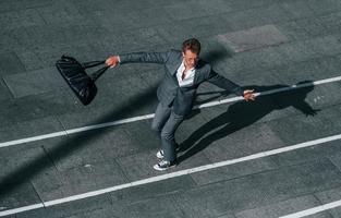 danser, célébrer le succès. jeune homme d'affaires en tenue de soirée grise est à l'extérieur de la ville photo