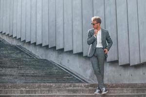 posant pour un appareil photo. jeune homme d'affaires en tenue de soirée grise est à l'extérieur de la ville photo