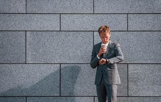 contre le mur gris. jeune homme d'affaires en tenue de soirée grise est à l'extérieur de la ville photo