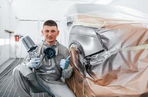 se trouve près d'une voiture fraîchement peinte. Réparateur automobile caucasien en uniforme travaille dans un garage photo