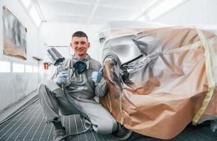 se trouve près d'une voiture fraîchement peinte. Réparateur automobile caucasien en uniforme travaille dans un garage photo