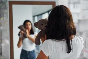 jeune femme tient un ours en peluche et se regarde dans le miroir photo