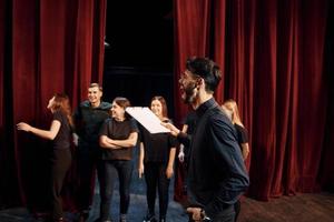 type expressionalible pratiquant son rôle. groupe d'acteurs vêtus de vêtements de couleur sombre en répétition au théâtre photo