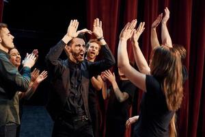 donner un high five, célébrer le succès. groupe d'acteurs vêtus de vêtements de couleur sombre en répétition au théâtre photo