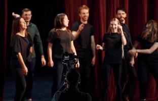 des gens heureux célébrant le succès. groupe d'acteurs vêtus de vêtements de couleur sombre en répétition au théâtre photo