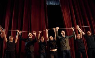 tenant la corde dans les mains au-dessus des têtes. groupe d'acteurs vêtus de vêtements de couleur sombre en répétition au théâtre photo