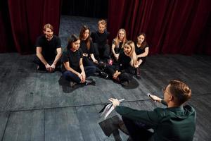 assis sur le sol. groupe d'acteurs vêtus de vêtements de couleur sombre en répétition au théâtre photo