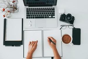 vue de dessus. jeune femme indépendante travaillant à l'intérieur du bureau pendant la journée. ordinateur portable et bloc-notes photo